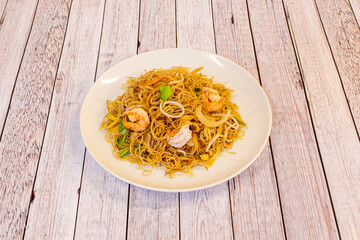 thin fried chinese rice noodles with prawns and vegetables sautéed in wok with soy sauce on white plate
