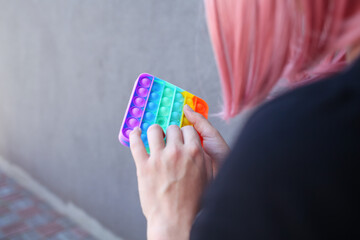 Girl with rainbow Pop It Fidget in hands. Teen Playing, Push bubble on Pop it Fidget.