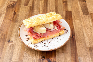 Italian focaccia with Iberian ham and cheese, black pepper and olive oil on wooden table