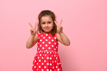 Joyful gorgeous 4 years Birthday baby girl in summer dress gesturing, doing victory sign with finger. Adorable child showing number two.