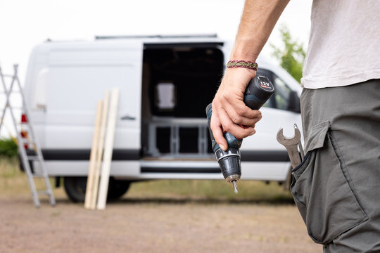 Electric screwdriver held by a hand and a van in the background