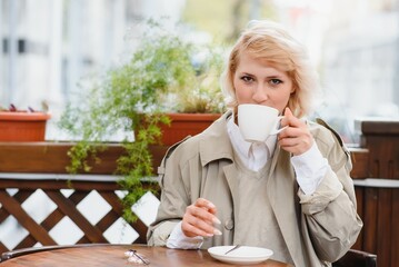 Fashion portrait of young woman siting at the table with cup of coffee, tea in street cafe.