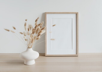 Wooden frame mockup on beige table, modern beige ceramic vase with dry grass.Neutral color. White wall background. Scandinavian interior. Copy space.