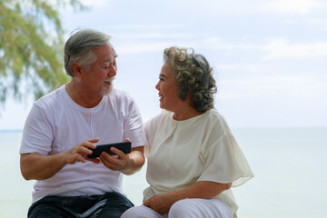 Happy Asian senior couple enjoy playing smartphone outdoor. Retirement and love concept.