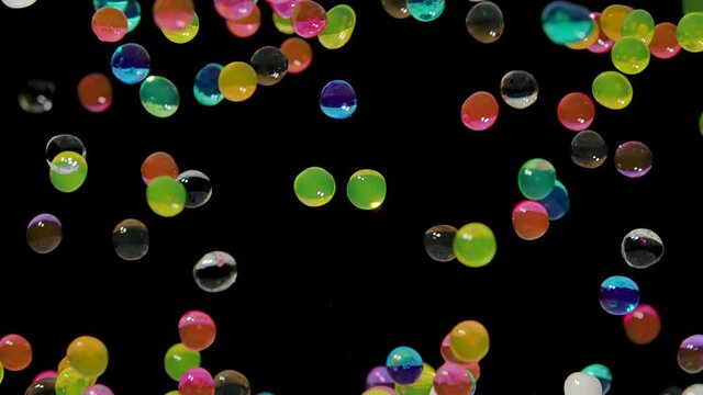 Many multicolored water gel balls move abstractly across the screen against a black background. Hydrogel balls orbeez bouncing and fly in different directions. Polymer superabsorbing gel. Close up