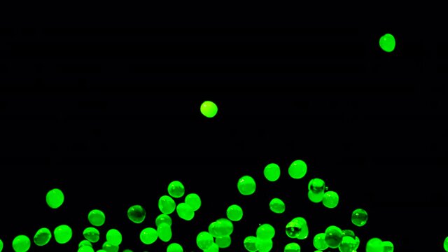 Bright green water gel balls bouncing against a black background. Polymer gel. Silica gel. Hydrogel balls bouncing and fly in different directions caused by sound vibrations. Close up. Slow motion.