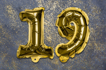 The number of the balloon made of golden foil, the number nineteen on a gray background with sequins. Birthday greeting card with inscription 19. Numerical digit, Celebration event, template.