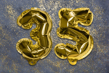 The number of the balloon made of golden foil, the number thirty-five on a gray background with...