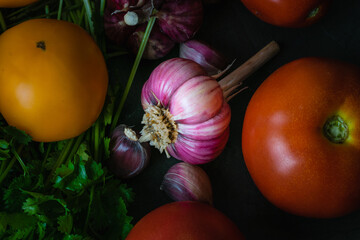 Lots of vegetables: garlic, cilantro, parsley and tomatoes on a dark countertop