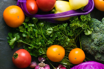Lots of vegetables: garlic, cabbage, broccoli, cilantro, parsley and tomatoes on a dark tabletop. Vegetables in a reusable fruit and vegetable bag. Ecology protection concept