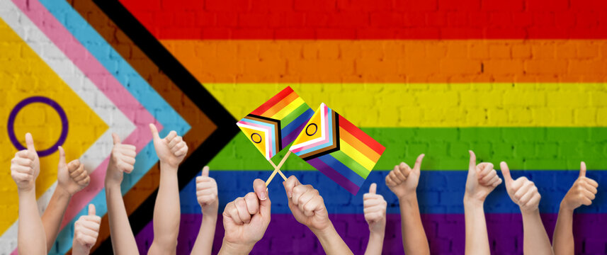 lgbtq, trans and intersex rights concept - multiracial human hands showing thumbs up over rainbow progress pride flag on background