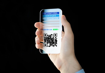 coronavirus, technology and health concept - close up of woman's hand holding and showing transparent smartphone with international certificate of covid-19 vaccination on screen over black background