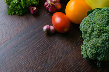 Vegetables broccoli, cilantro, tomatoes, peppers, garlic, zucchini, cabbage on a dark wooden table top. The concept of vegetarianism and proper nutrition.