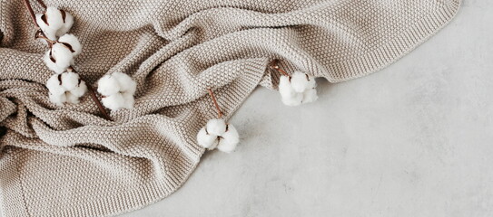 Beige knitting blanket and dry cotton flowers on gray background top view with copy space....