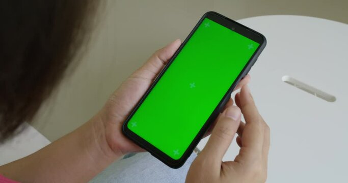 Close up of a woman's hand holding a mobile telephone with green screen in home. Top view chroma key smartphone technology, cell phone holding by hand concept. 