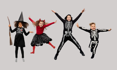 halloween, holiday and childhood concept - happy children in carnival costumes jumping over grey background