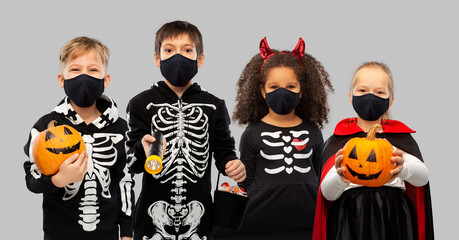 holiday, health and pandemic concept - children in halloween costumes and black reusable masks trick-or-treating over grey background