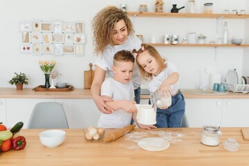 Fototapeta na wymiar An attractive smiling family of mother, and two children, boy, girl, son, daughter cookies in a kitchen at home