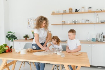 Happy young mother with cute little preschooler kids have fun making dough baking pie or pastry in modern kitchen together, overjoyed mother teach small children doing bakery cooking at home