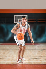 Dark-haired athletic man playing basket-ball in the gym