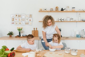 An attractive smiling family of mother, and two children, boy, girl, son, daughter cookies in a kitchen at home