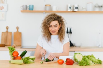Obraz na płótnie Canvas Happy young housewife mixing vegetable salad