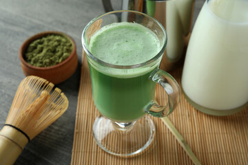 Cup of matcha latte and accessories for making on gray textured table