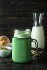 Glass jar of matcha latte and accessories for making on wooden background