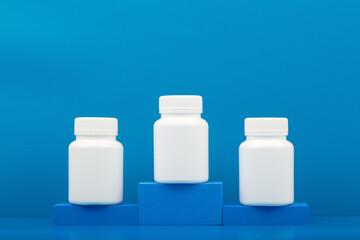 Creative composition with three white medication bottles on winner pedestal against blue background with copy space. Concept of medical treatment, vitamins and pharmaceutical industry