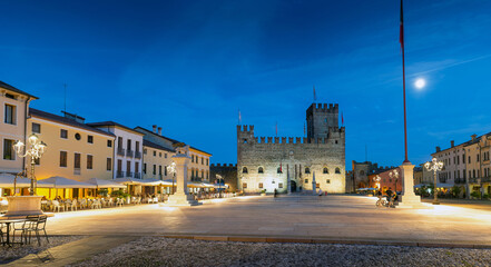 Marostica, Italy - Chess square in the evening. People sitting at the tables of the bars in the square. In the background the medieval castle 
