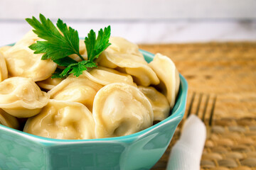 Meat dumplings with herbs in a turquoise bowl with a golden fork on a straw serviette on a light background close-up with a place for text