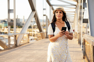 Travel woman at the bridge. Young beautiful woman using the phone. Beautiful woman traveling around the city.