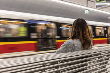 Train blurred by the speed with lonely woman in front sitting and waiting for right train in a...