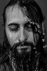 Black and white close-up portrait of a young bearded man with closed eyes with streams of water running down his face