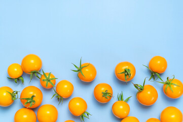 Ripe fresh yellow orange tomatoes with green tails on blue background flat lay top view. Cherry tomatoes. Vegetables, healthy vegan organic food, harvest concept, tomatoes pattern layout, cooking