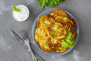 Fritters from zucchini in grey plate with sour cream sauce and greens. Vegetable pancakes of courgettes with green salad