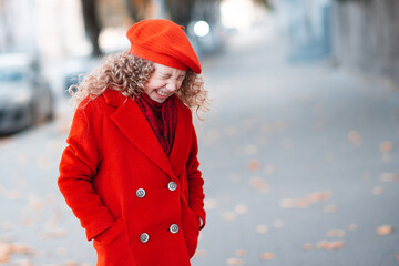 Stylish happy kid girl 5-6 year old with blonde curly hair wear red color jacket and beret hat walk in city street. Autumn season. Childhood. Laughing funny toddler outdoors.