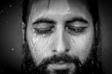 Black and white very close-up portrait of a young bearded man with closed eyes with streams of...