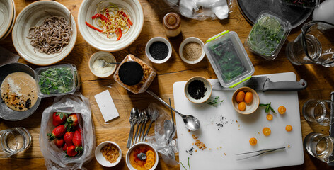 A table on which products for cooking and decorating dishes prepared for a photo shoot are arranged in a chaotic manner. Copy space