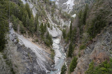 Canyon or ravine called Ruinaulta on Anterior Rhine river in Switzerland. A detail in high angle view. Clear blue water stream with stone banks is between tall rocky walls partly covered by conifers. 