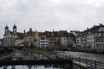 Fototapeta na wymiar Lucerne, Switzerland 04 17 2021: Waterfront of Lucerne, old city along bank of the river Reuss, with dominant Jesuit church.