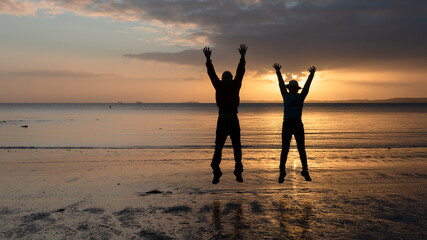 Silhouette image of two people jumping in the air at Milford Beach, Auckland