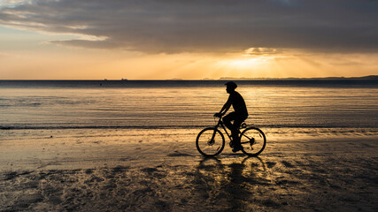 Obraz premium Silhouette of a man bike riding on the sand beach at sunrise