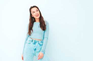 Young beautiful smiling female in trendy summer hipster clothes. Sexy carefree woman posing near light blue wall in studio. Positive model having fun indoors. Cheerful and happy