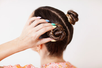 Naklejka premium A young woman fixes her hair bun. She wears rainbow gradient manicure.