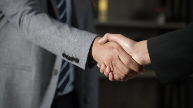 business partner shakes hands to join the business with a sunset, two colleagues shaking hands in the office against the background of a window and sunbeam. Tracking shot in slow motion.