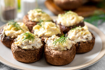 Stuffed mushroom champignons with cream cheese, chicken fillet and parmesan in a plate on the light gray kitchen table closeup 