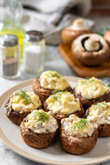 Stuffed mushroom champignons with cream cheese, chicken fillet and parmesan in a plate on the light gray kitchen table closeup 