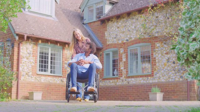 Smiling mature couple with man sitting in wheelchair being pushed by woman outside home - shot in slow motion