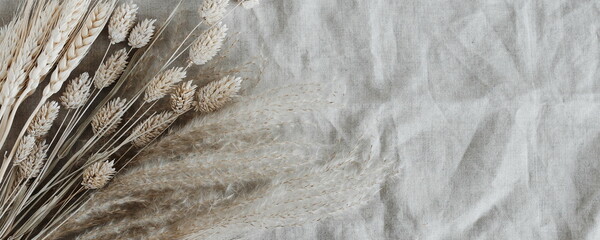 Dry beige grass plant bouquet top view on beige linen fabric texture banner.Flowers background . Copy space.